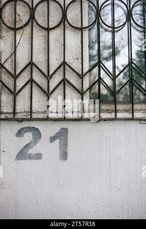 Die Zahl 21 ist mit einer Schablone auf eine graue Wand unter einem Fenster mit Gittern gemalt. Hausnummer 21 Stockfoto