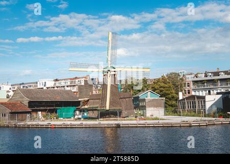 Historische Windmühle am Ufer eines Kanals in einer der schönsten Städte Hollands, Amsterdam. Landschaft der Stadt bei Sonnenuntergang. Stockfoto