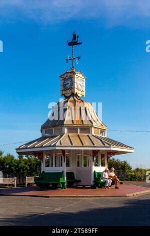 Unterschlupf und Uhrenturm an der Promenade über der Viking Bay in Broadstairs, Thanet, Kent, England, Großbritannien, mit älteren Ehepaaren auf der Bank, die Bücher lesen. Stockfoto