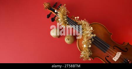 Violine mit rotem Hintergrund, verziert mit Lametta und goldenen Weihnachtskugeln. Draufsicht. Stockfoto