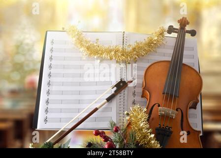 Weihnachtliches religiöses Violinmusikkonzept mit Geige mit weihnachtsdekoration und Noten mit religiösem Tempel Hintergrund. Vorderansicht. Stockfoto