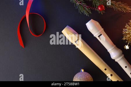 Zwei traditionelle Kunststoffrecorder für Kindermusik auf einem schwarzen Tisch mit Weihnachtsdekoration. Draufsicht. Stockfoto