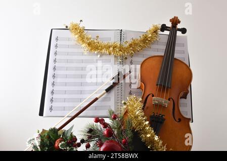 Weihnachtliches religiöses Violinmusikkonzept mit Geige mit weihnachtsdekoration und Noten mit weißem isoliertem Hintergrund. Vorderansicht. Stockfoto