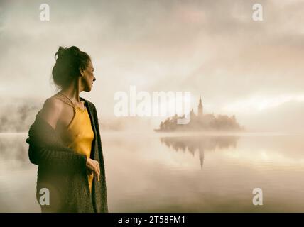 Frau im grauen Mantel, die einen Sonnenaufgang im Nebel am Ufer des Bleder Sees beobachtet, Slowenien IV Stockfoto