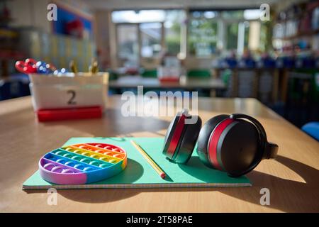 Ohrenschützer oder Kopfhörer und zappeln Spielzeug, um Kindern mit ASD oder Autismus auf dem Tisch im Schulunterricht zu helfen Stockfoto