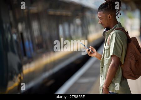 Junger Mann Pendelt Auf Dem Zug Zur Arbeit, Steht Auf Dem Bahnsteig Und Sieht Sich Das Handy An, Wenn Der Zug Kommt Stockfoto