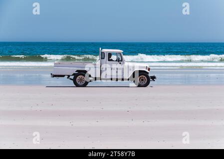 Ein alter weißer Pick-up-Truck fährt entlang des weißen Sandstrandes in Elands Bay in Südafrika Stockfoto