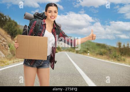 Eine junge Frau per Anhalter und mit einem leeren Pappschild auf der Straße Stockfoto