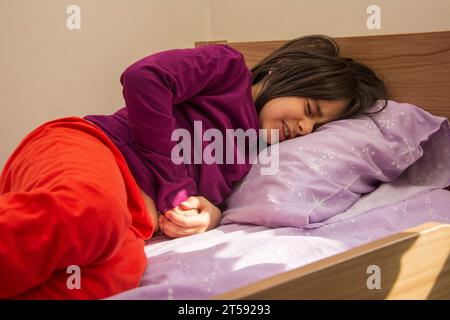 Kleines Mädchen, das mit Bauchschmerzen im Bett liegt Stockfoto
