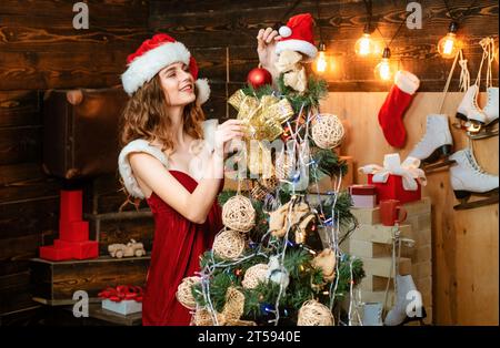 Beauty Model Mädchen in Santa hat auf Home Design dekorieren. Freundlich und Freude. Glückliche Menschen. Weihnachtsdekoration und Geschenkbox auf hölzernem Hintergrund. Richtig Stockfoto