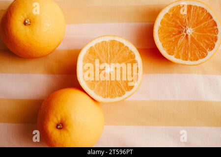 Die Hälften reifer, süßer Orangen sind auf einem gestreiften orangefarbenen Hintergrund angeordnet. Der Sommer und frisches Obst. Die gesunde Ernährung und Ernährung, die Förderung der Stockfoto