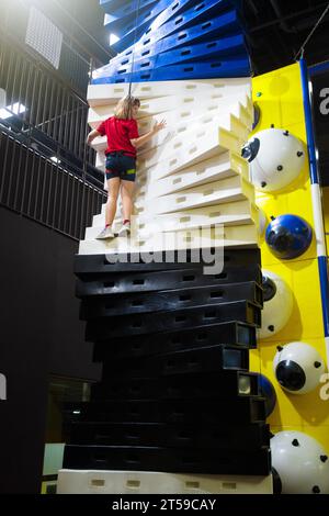 Kinderklettern im Vergnügungspark. Boulderspaß auf Kindergeburtstag. Indoor-Spielplatz mit Kletterwand. Gesunde Aktivität für Kinder. Stockfoto