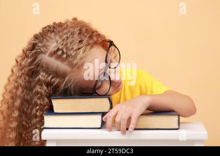 Zurück zur Schule. Müde Schülerin in Brille schläft auf einem Buch am Schreibtisch, wurde vom Studium müde, schlief ein, während Hausaufgaben gemacht, gelesen oder gesiegt wurde Stockfoto