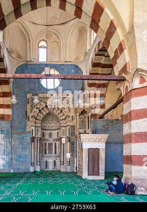 Kairo, Ägypten - 27. November 2021: Mihrab und verzierte Marmor-Minbar vor blauen Iznik-Keramikfliesen, eingerahmt von einem großen Bogen, in der historischen Moschee der Mamluk-Ära der Aqsunqur-Blauen Moschee Stockfoto