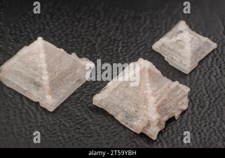 Nahaufnahme von drei Pyramidensalzkristallen auf dunklem, strukturiertem Hintergrund. Stockfoto