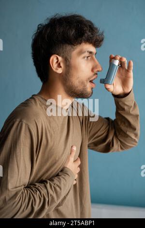 Porträt eines arabischen jungen Mannes mit Asthma-Inhalator vor blauem Hintergrund zu Hause Stockfoto