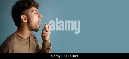 Arabischer junger Mann mit Kehlspray isoliert auf blauem Hintergrund. Banner. Stockfoto