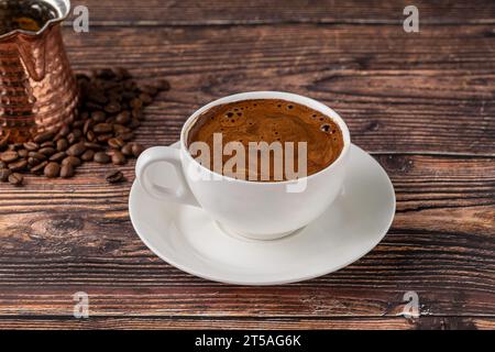 Doppelter türkischer Kaffee in einer weißen Porzellantasse mit dekorativer Kaffeekanne auf einem Holztisch Stockfoto