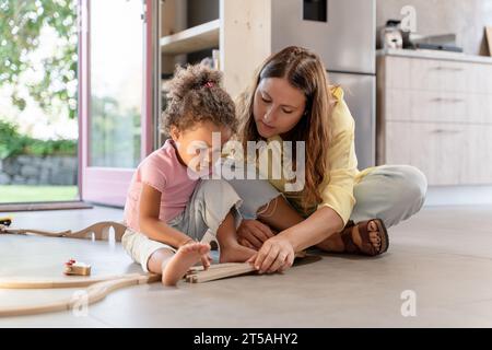 Mutter und Kind spielen mit Spielzeugzug - Eine Mutter und ihre birassische Tochter bauen ein hölzernes Zugset zusammen, eine herzerwärmende Szene der Familienbindung und p Stockfoto