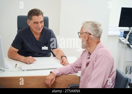 Der behandelnde Arzt kommuniziert mit einem alten Mann in der Arztpraxis Stockfoto