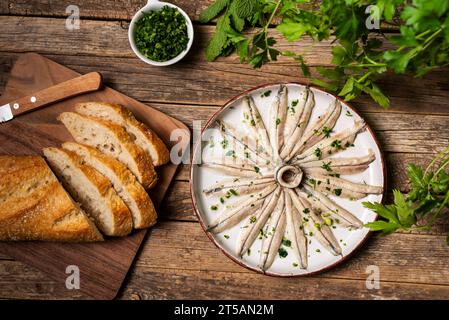 Rustikales Gericht mit Sardellen in Essig, gewürzt mit Knoblauch und Petersilie, zusammen mit einigen Brotscheiben auf einem alten Holztisch. Stockfoto