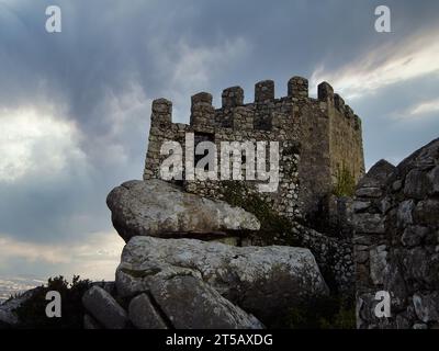 Wachtturm und Verteidigungsmauer im mittelalterlichen Castelo dos Mouros, auch bekannt als Schloss der Mauren in Sintra, Portugal. Abenddämmerung und Sturm bedeckter Himmel Stockfoto