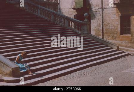 Frau aus den 1950er Jahren im Urlaub in Girona, Katalonien, Spanien, ruht auf der großen Steintreppe, die zur Kathedrale von Girona führt. 1959 Stockfoto