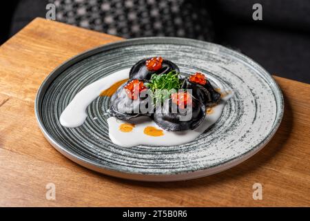 Ravioli mit Tonne, Kaviar und Bechamelsauce. Schwarze Pelmeni, Knödel auf Teller. Traditionelle russische Küche. Stockfoto