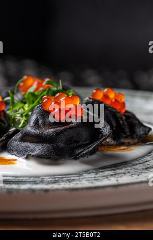 Ravioli mit Tonne, Kaviar und Bechamelsauce. Schwarze Pelmeni, Knödel auf Teller. Traditionelle russische Küche. Stockfoto