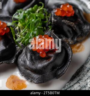 Ravioli mit Tonne, Kaviar und Bechamelsauce. Schwarze Pelmeni, Knödel auf Teller. Traditionelle russische Küche. Stockfoto