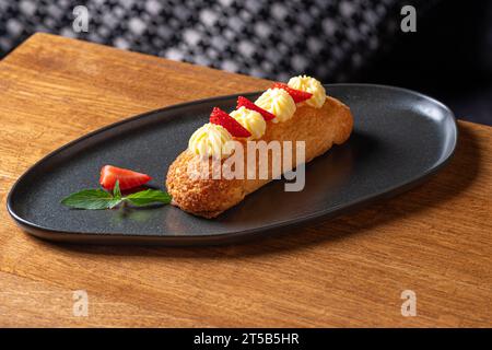 Eclairs mit Sahne und Erdbeeren auf einem Teller. Nahaufnahme auf dem Tisch, serviert in einem Restaurant, Menü-Food-Konzept. Stockfoto