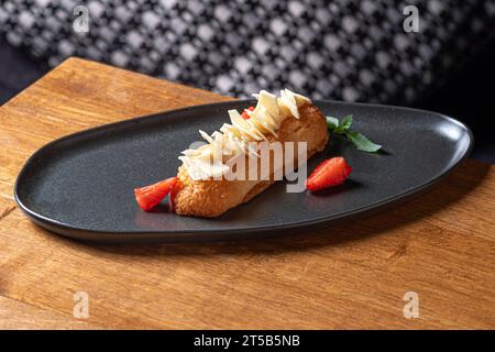 Eclairs mit Sahne und Erdbeeren auf einem Teller. Nahaufnahme auf dem Tisch, serviert in einem Restaurant, Menü-Food-Konzept. Stockfoto