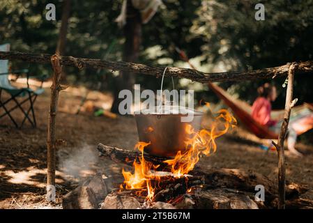 Fahren Sie mit einem Wasserkocher über ein brennendes Feuer auf dem Fluss und den Sonnenuntergang. Kochen über einem Lagerfeuer. Stockfoto