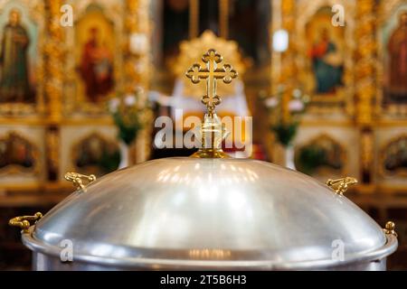 Kirchtafel aus Aluminium, große Schüssel, mit goldenem Kreuz und heiligem Wasser für die Taufe von Babys im orthodoxen Kirchentempel, Taufzeremonie. Concep Stockfoto