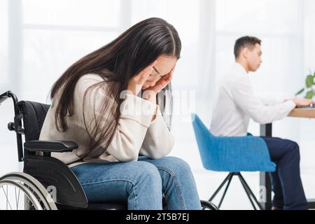 Frustrierte junge Frau mit Kopfschmerzen sitzender Rollstuhl-Geschäftsmann im Büro Stockfoto