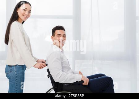 Porträt lächelnde junge Frau stehender Mann sitzender Rollstuhl, der Kamera aussah Stockfoto