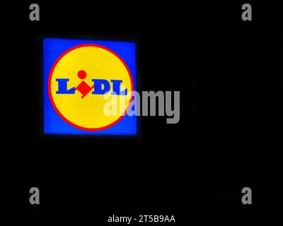 Ein hell beleuchtetes Schild mit dem Firmenlogo des deutschen Discount-Supermarktes Lidl. Nachts mit schwarzer Einfassung aufgenommen. Stockfoto