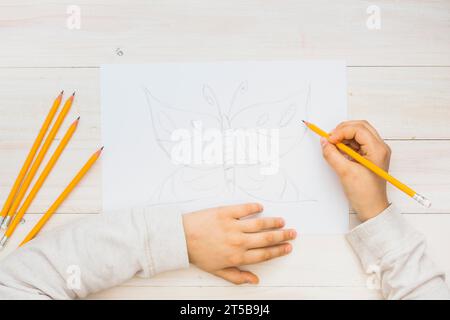 Kind Hand skizziert Schmetterling mit Bleistift Holz Hintergrund Stockfoto