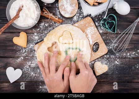 Hände, die Valentinstag-herzförmige Kekse mit Küchenutensilien machen Stockfoto