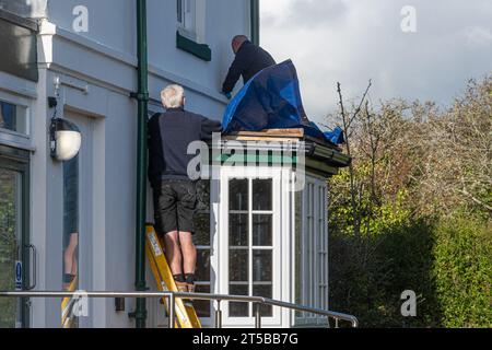 Der Sturm Ciaran traf die Südküste Englands Anfang November 2023 mit starken Winden und starkem Regen, was örtlich begrenzte Überschwemmungen und Sachschäden verursachte. Am 3. November 2023, einen Tag nach dem Herbststurm bei Hill Head bei Fareham, Hampshire, England, machen zwei Männer eine vorübergehende Reparatur an einem undichten Grundstück mit einer Plane. Stockfoto