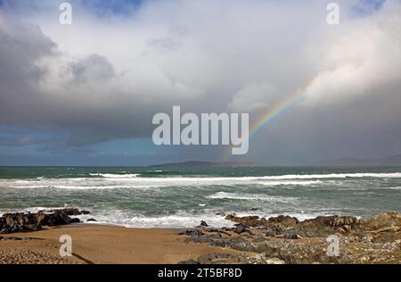 Ein Blick auf eine felsige Küste mit eintretender Flut und Regenbogen in Richtung des Sound of Taransay auf der Isle of Harris, Äußere Hebriden, Schottland. Stockfoto