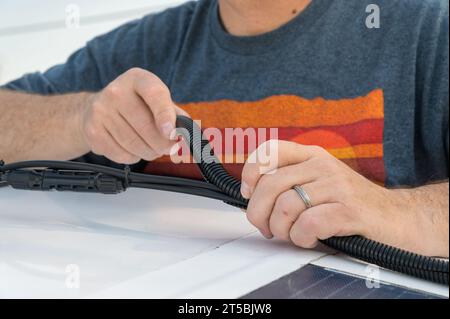 Mann, der einen Kabelkanal mit geteiltem Draht für die Kabelverbindungen eines Solarmoduls installiert Stockfoto