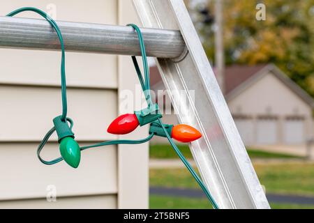 WeihnachtsLichter hängen an der Leiter, die draußen vor dem Haus stand. Weihnachtsbeleuchtung Dekoration, Leitersicherheit und Unfallverhütungskonzept. Stockfoto