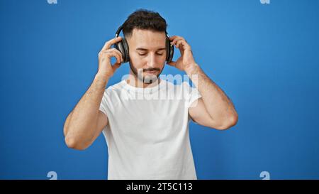 Junger araber, der Musik vor einem isolierten blauen Hintergrund hört Stockfoto