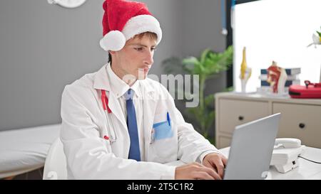 Junger kaukasischer Männerarzt, der weihnachtshut trägt, arbeitet in der Klinik Stockfoto