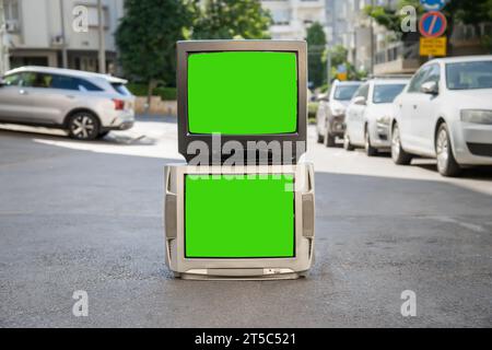 Zwei alte Fernsehgeräte mit einem grünen Bildschirm auf der Stadtstraße mit Autos Stockfoto