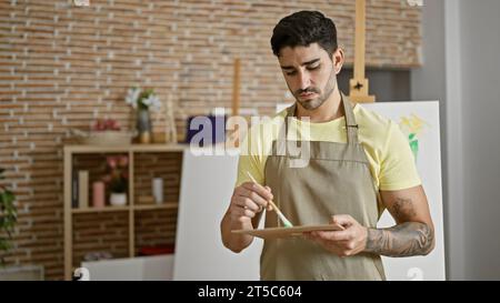 Junger hispanischer Künstler, der im Kunststudio Farbe auf Palette mischt Stockfoto