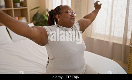 Selbstbewusste afroamerikanische Frau, lächelnd, genießt morgens die Dehnung auf ihrem bequemen Bett und entspannt sich drinnen Stockfoto