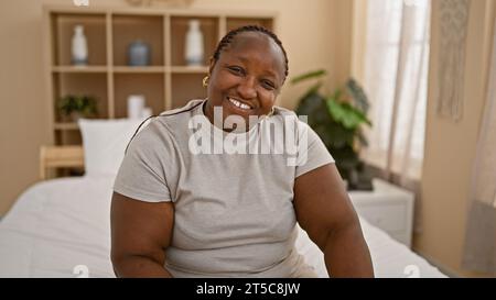 Strahlende afroamerikanische Frau genießt einen entspannten Morgen und lächelt selbstbewusst auf ihrem gemütlichen Schlafzimmerbett. Stockfoto