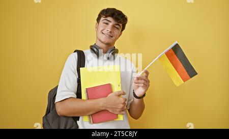 Selbstbewusster junger hispanischer Mann, ein deutscher Student, steht zwanglos mit Freude und hält Bücher, deutsche Nationalflagge, isoliert auf gelbem Hintergrund Stockfoto